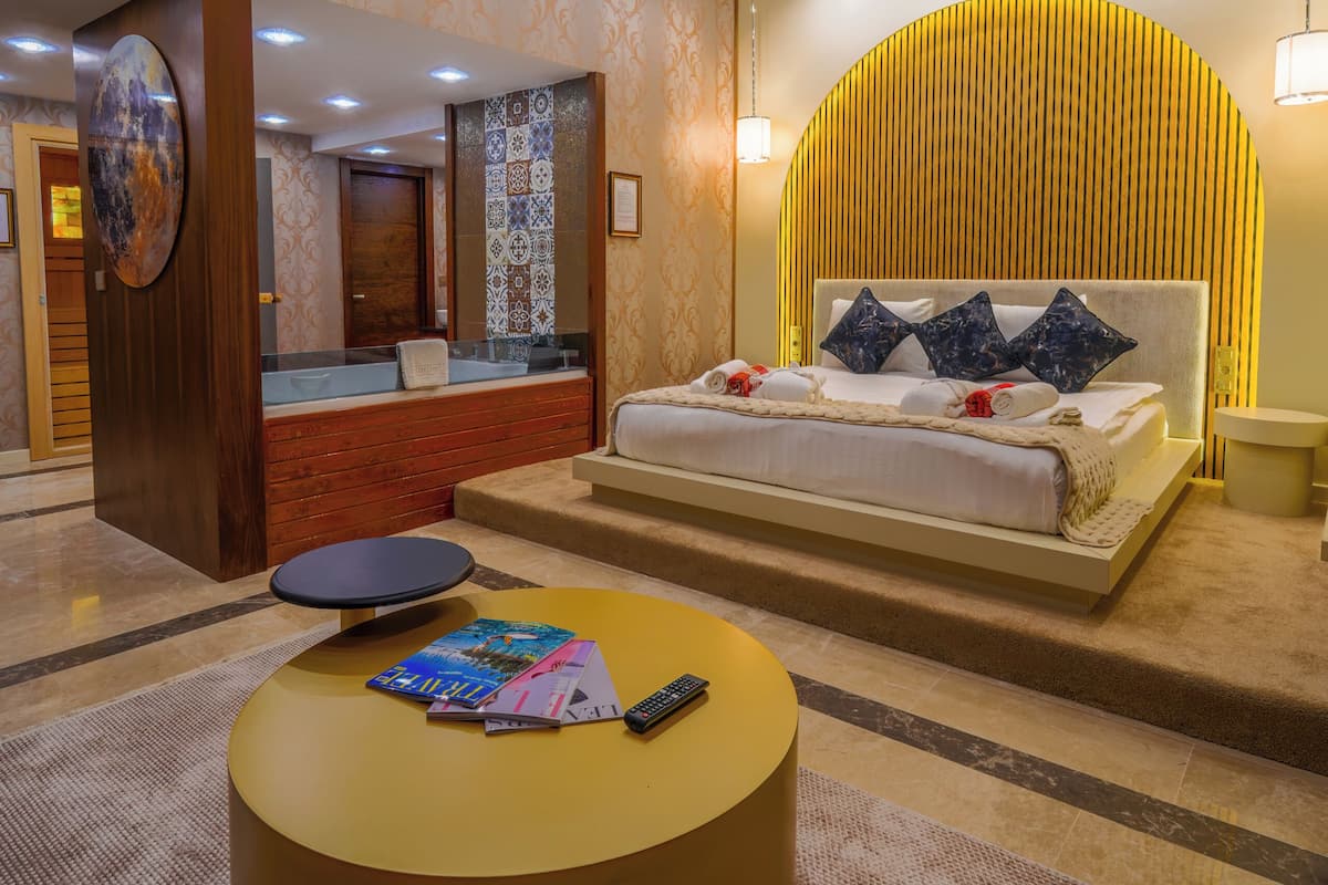 A hotel room with a bed, a round coffee table, a bathroom with a mirror, and a reception area.