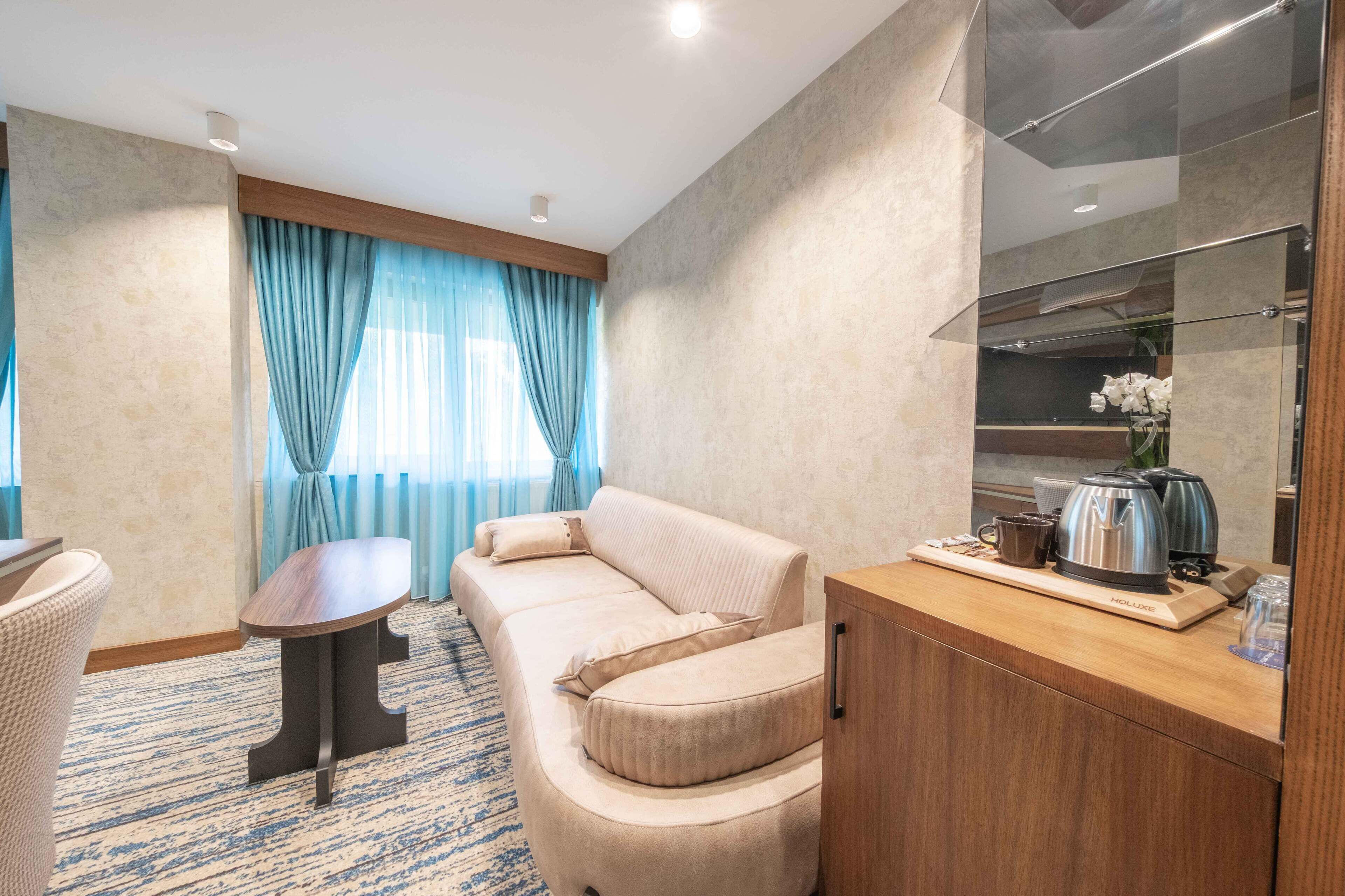 A modern hotel room with a sofa, a small table, a cabinet, and a window with curtains.