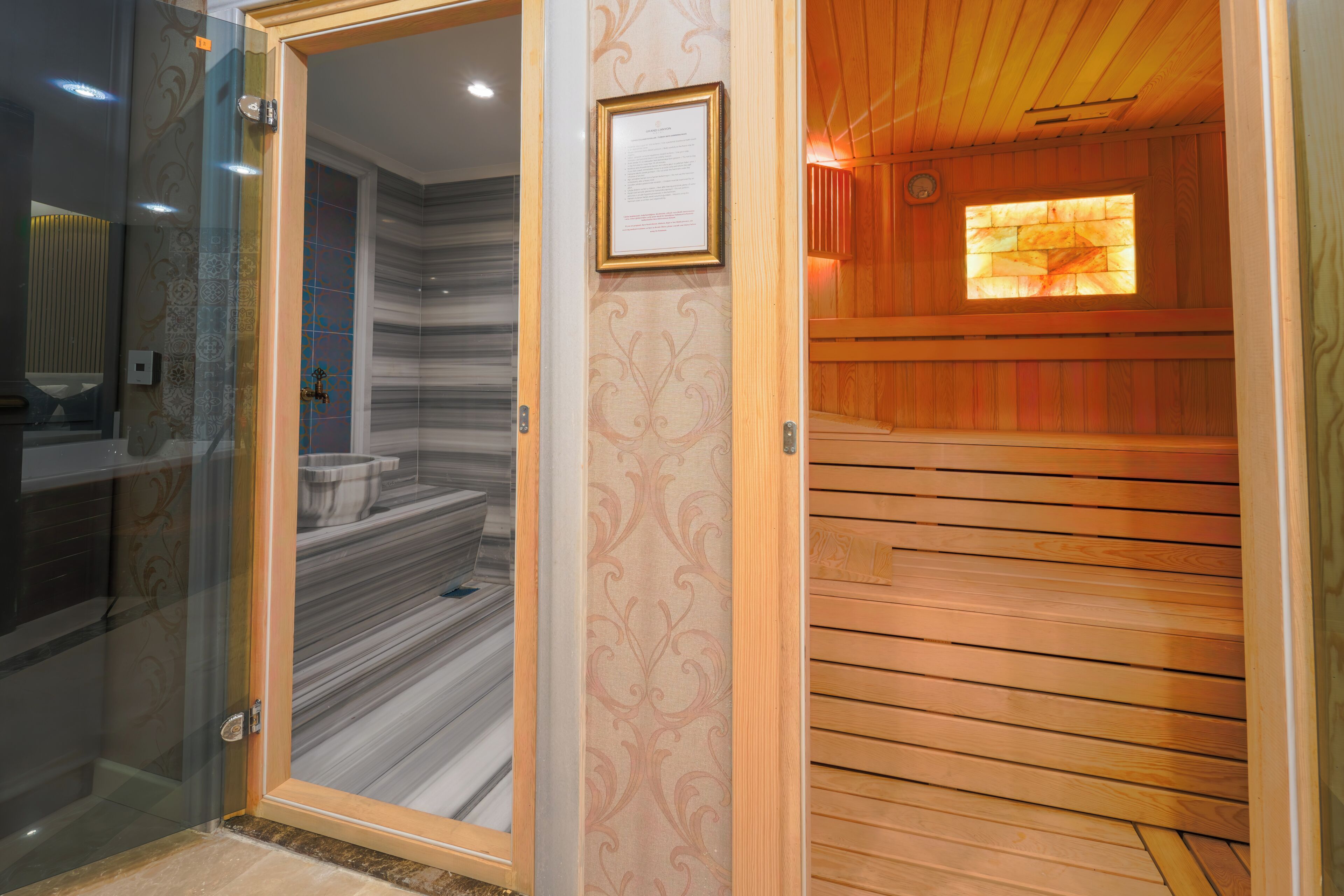 A sauna room with a wooden floor, a glass door leading to a bathroom, and a framed certificate on the wall.