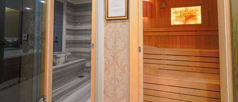 A sauna room with a wooden floor, a glass door leading to a bathroom, and a framed certificate on the wall.