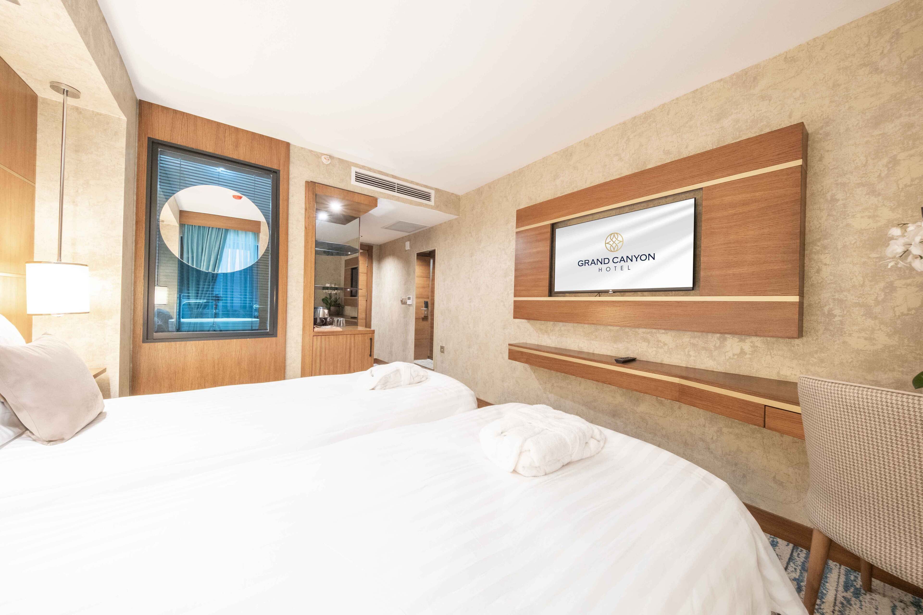 Habitación de hotel con cama, televisor montado en la pared, espejo y ventana con cortinas.