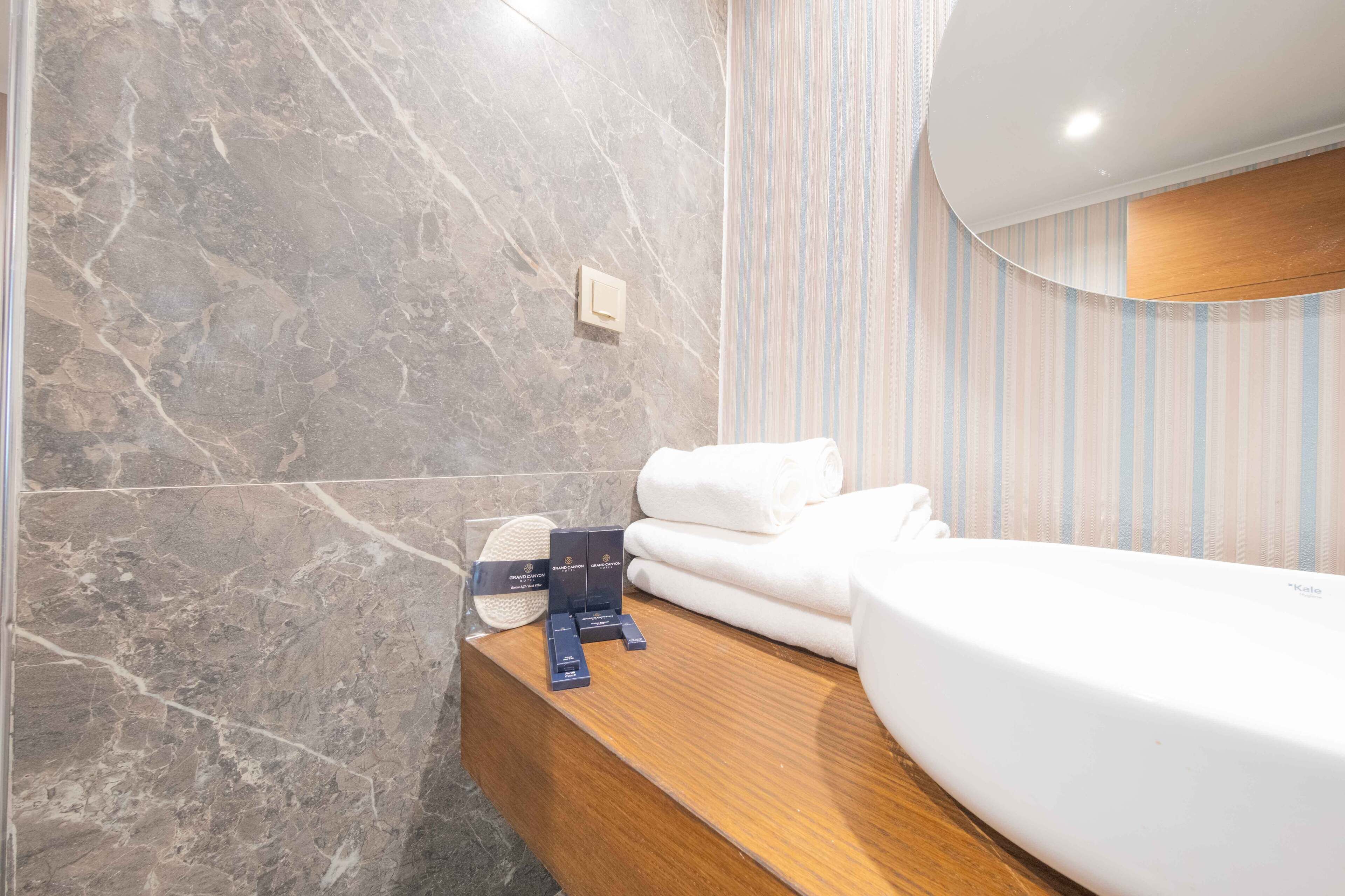 A bathroom with a marble wall, a wooden vanity, a white sink, and a striped towel rack.