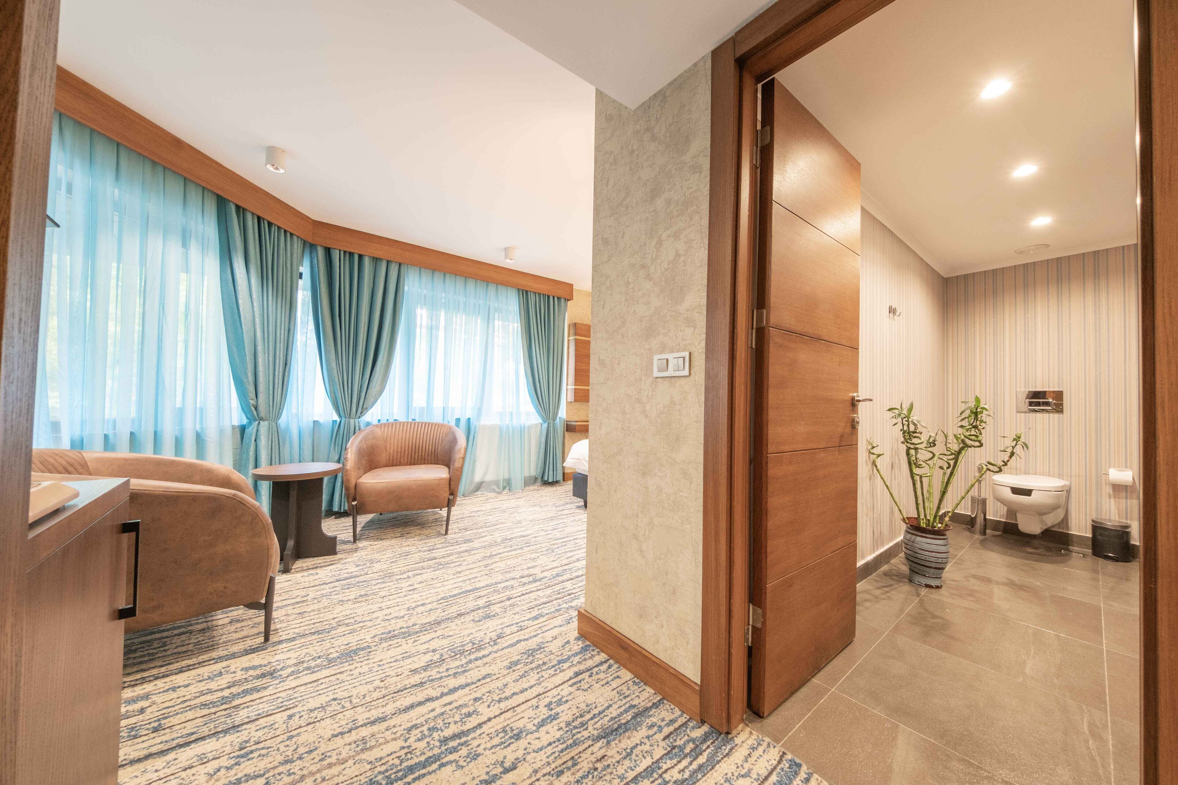 A hotel room with a sofa, armchair, small table, and a potted plant.
