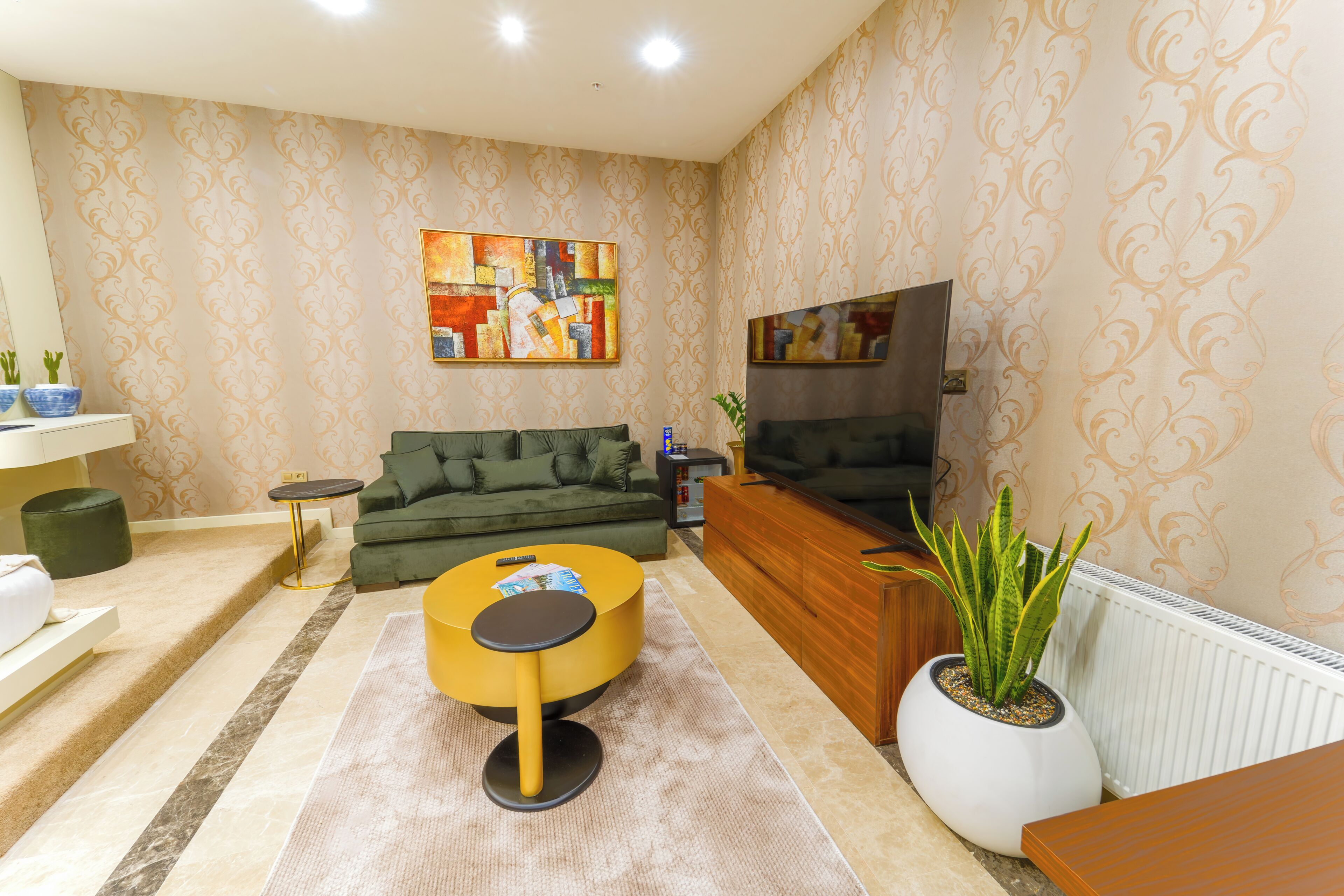 A living room with a green sofa, a yellow coffee table, a flat-screen TV, and a potted plant.