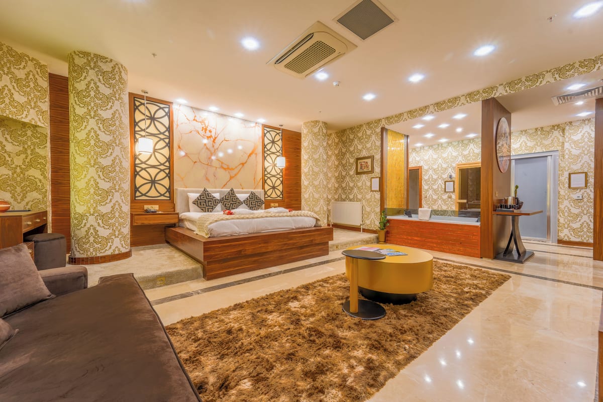 A modern hotel room with a bed, a sofa, a round coffee table, and a reception desk.