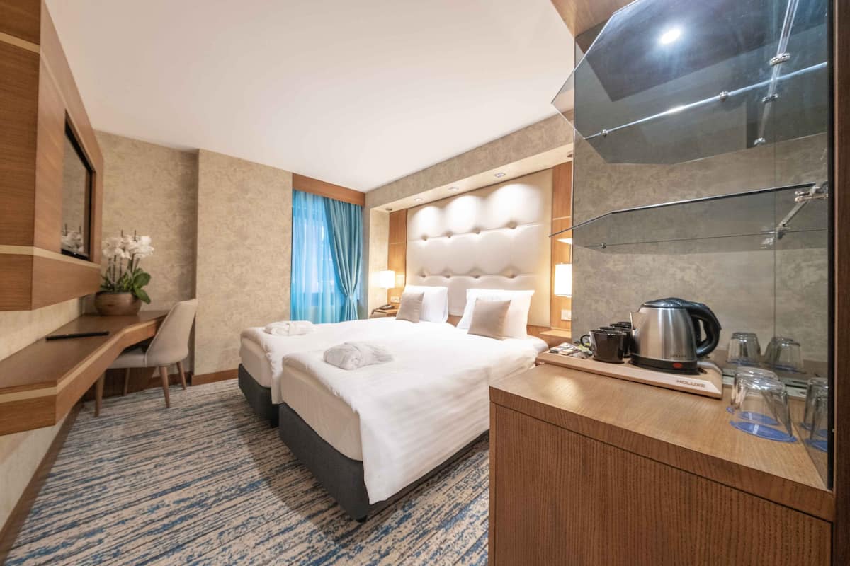 A hotel room with a large bed, a desk, a chair, a coffee maker, and a mirror.