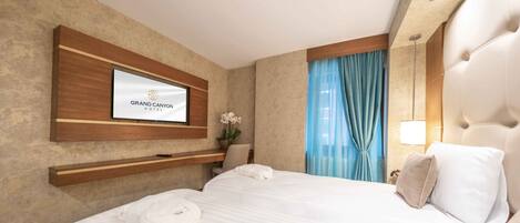 Una habitación de hotel con cama, televisor montado, mesita de noche y ventana con cortinas.