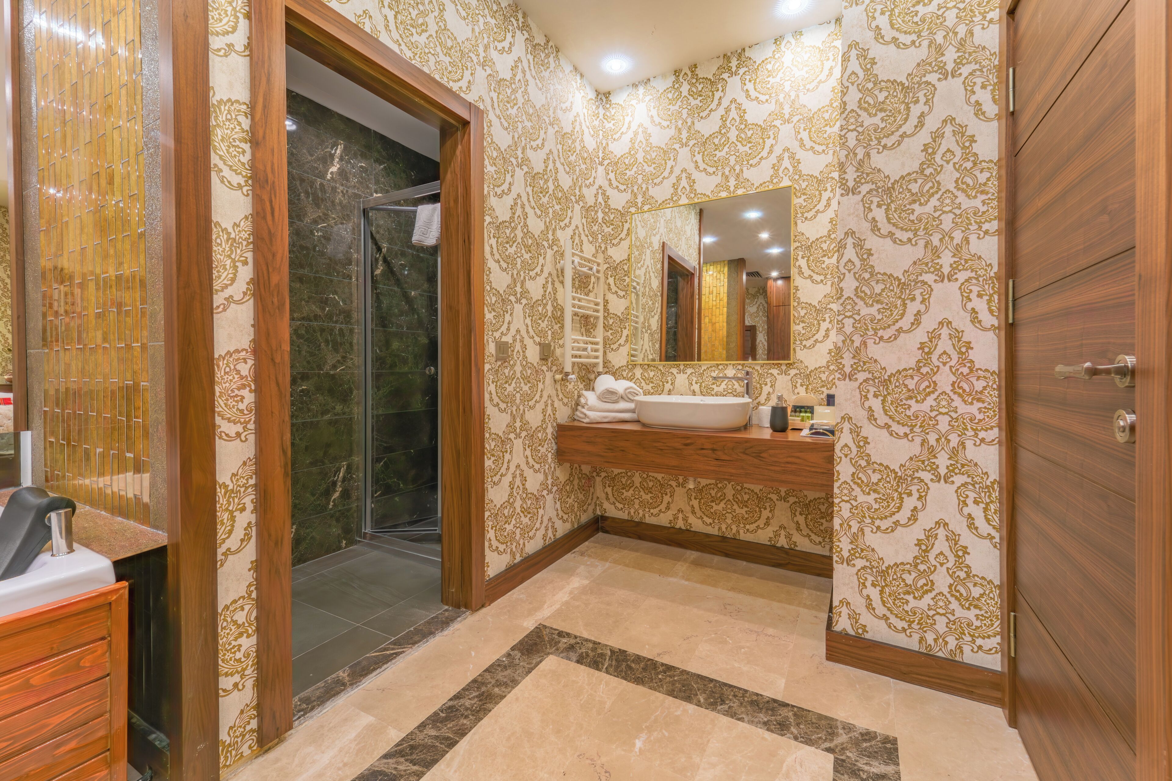 A bathroom with a shower, a sink with a mirror, and patterned wallpaper.