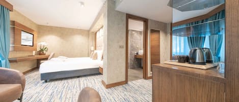 A hotel room with a bed, a desk, a chair, a bathroom, and a kitchenette.