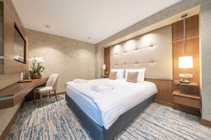 Habitación de hotel moderna con una cama grande, un escritorio, una silla y una mesita de noche con lámpara.