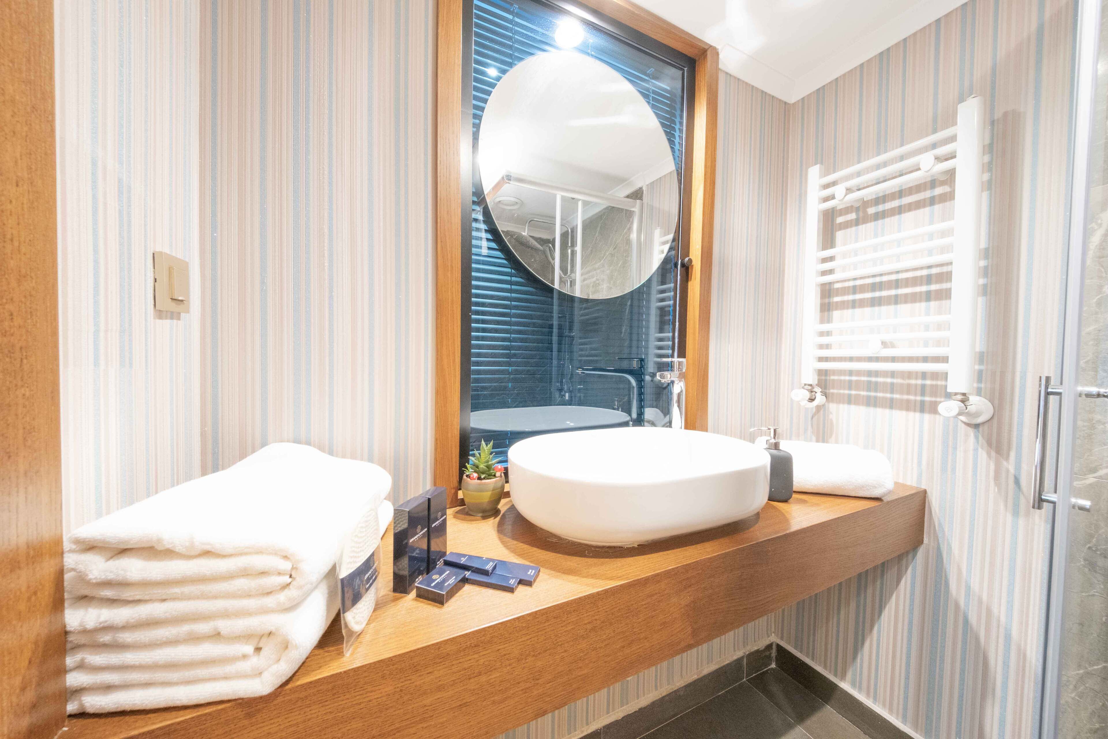 A modern bathroom with a wooden vanity, a round mirror, and a built-in sink.