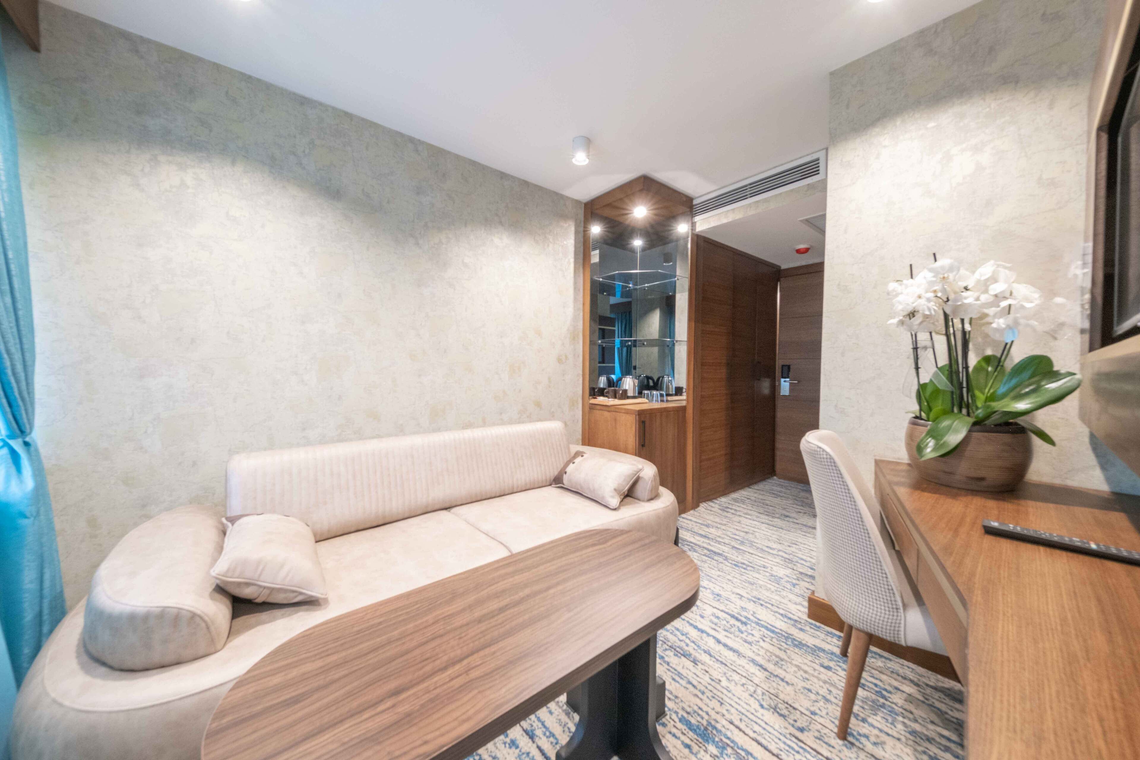 Una habitación de hotel moderna con un sofá, un escritorio de madera, una silla y una planta en maceta.