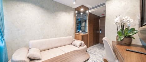 Una habitación de hotel moderna con un sofá, un escritorio de madera, una silla y una planta en maceta.
