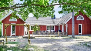 A red barn with a covered patio area, a swing set, and a gravel ground.