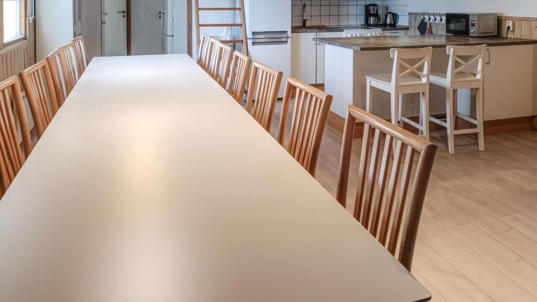 Ein langer Esstisch mit Holzsesseln, eine Küchenzeile inklusive Mikrowelle und Kühlschrank.