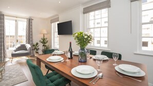A dining area with a wooden table set for four, surrounded by green upholstered chairs. A vase with flowers is on the table, and a bottle of wine is also visible. - Crescent Mews Apartment (Bath)