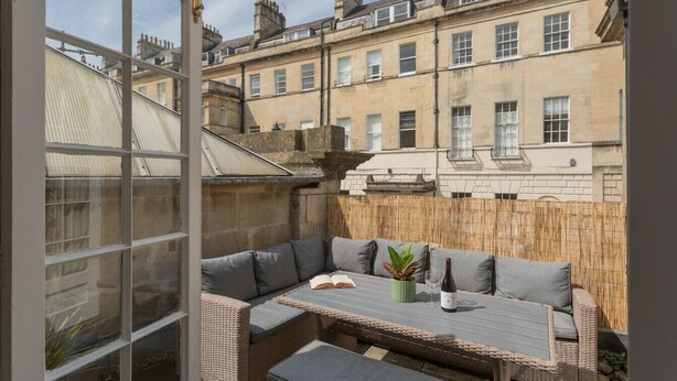 A cozy outdoor seating area with a table and cushions, overlooking a row of terraced houses. - Crescent Mews Apartment (Bath)