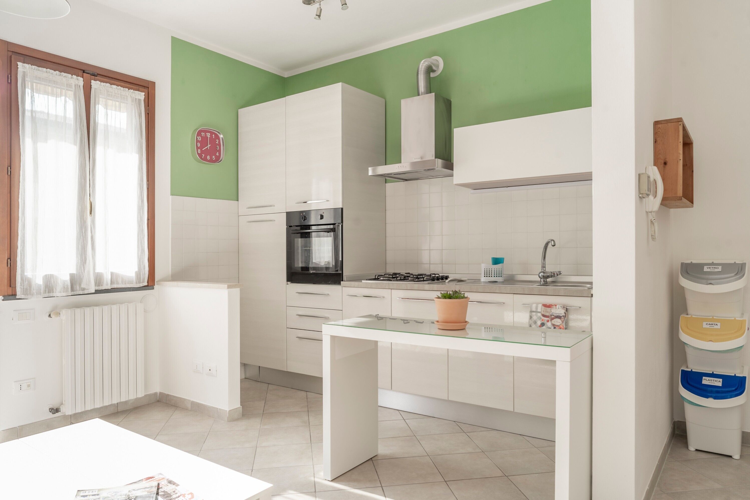 A modern kitchen with white cabinets, a gas stove, a built-in oven, and a window with sheer curtains.