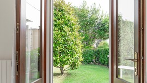 Blick durch eine Glastür in einen Garten mit Baum und Hecke.