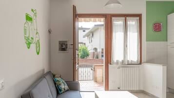 Una habitación con sofá, mesa, ventana con cortinas, radiador y un reloj de pared.