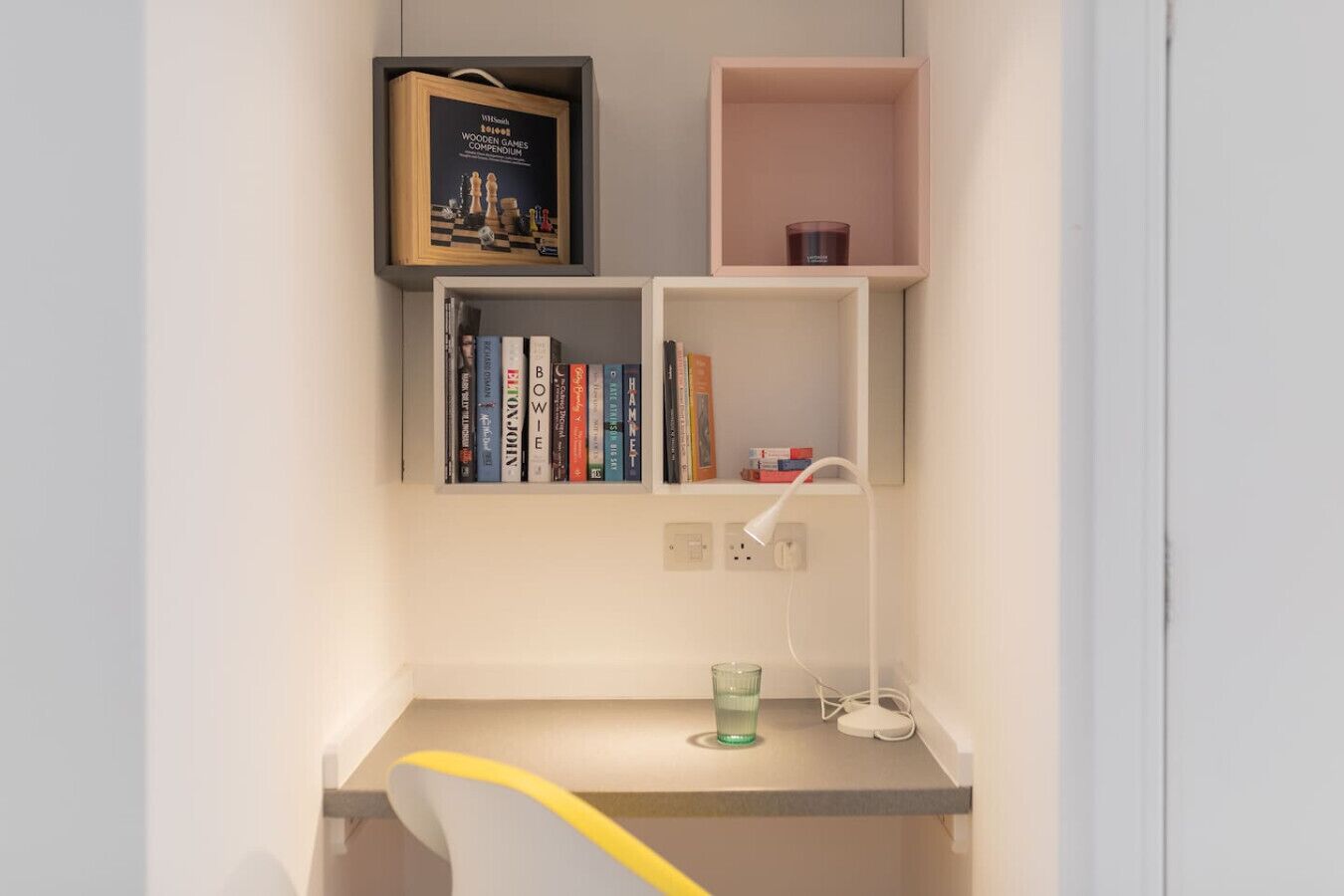 Ein Arbeitsbereich mit Schreibtisch, Bücherregalen, einer Lampe und einer Tasse.