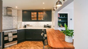 A kitchen with dark cabinetry, white subway tiles, a wooden countertop, and a herringbone-patterned floor. - Georgian Apartment near Royal Crescent (Bath and North East Somerset)