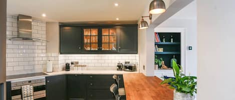 A kitchen with dark cabinetry, white subway tiles, a wooden countertop, and a herringbone-patterned floor.