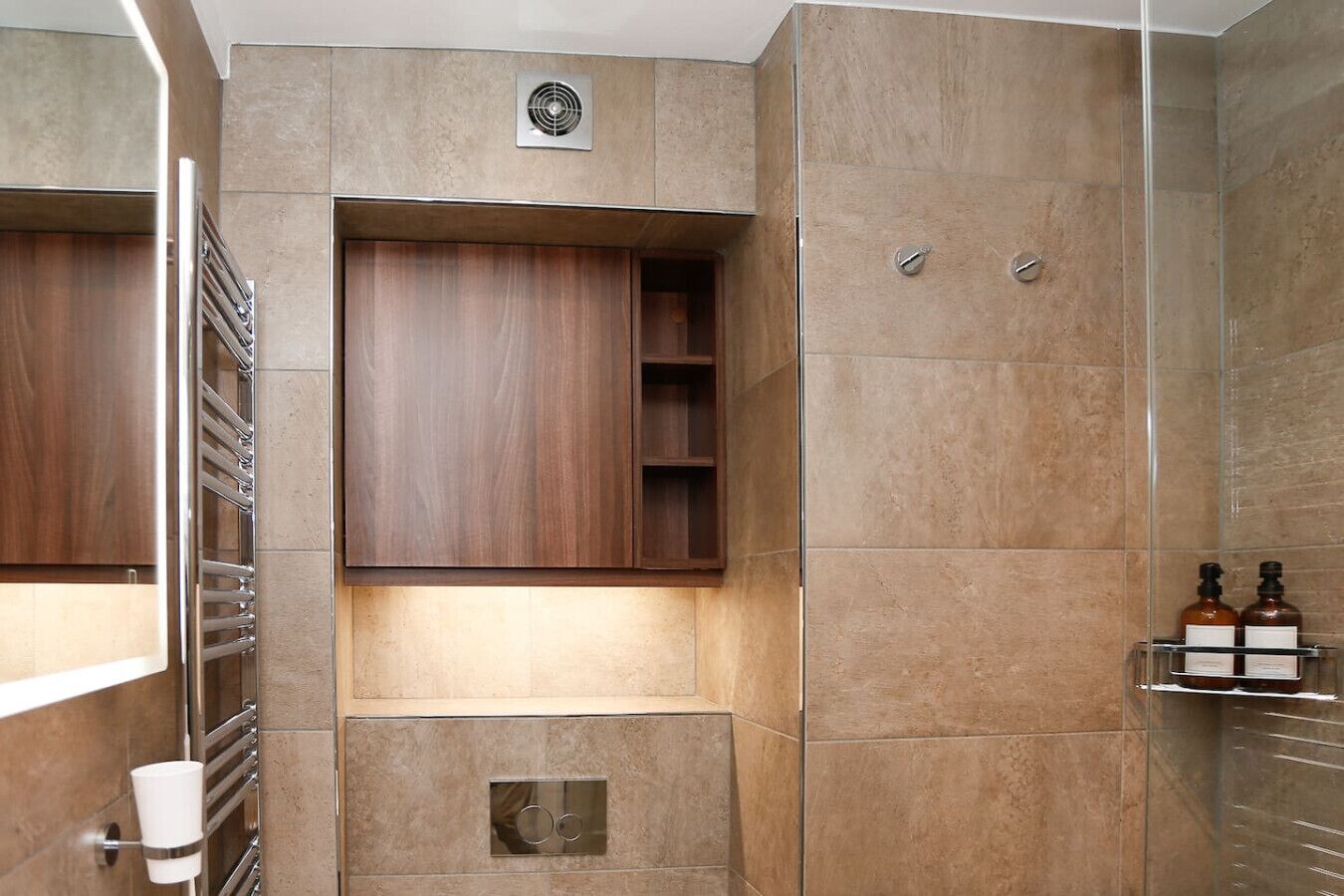Une salle de bain moderne dotée d’un meuble-lavabo en bois intégré, d’une cabine de douche en verre et d’une étagère murale pour les articles de toilette.
