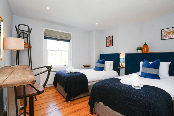 Une chambre d’hôtel avec deux lits, un bureau, une chaise, une fenêtre et un tableau au mur.