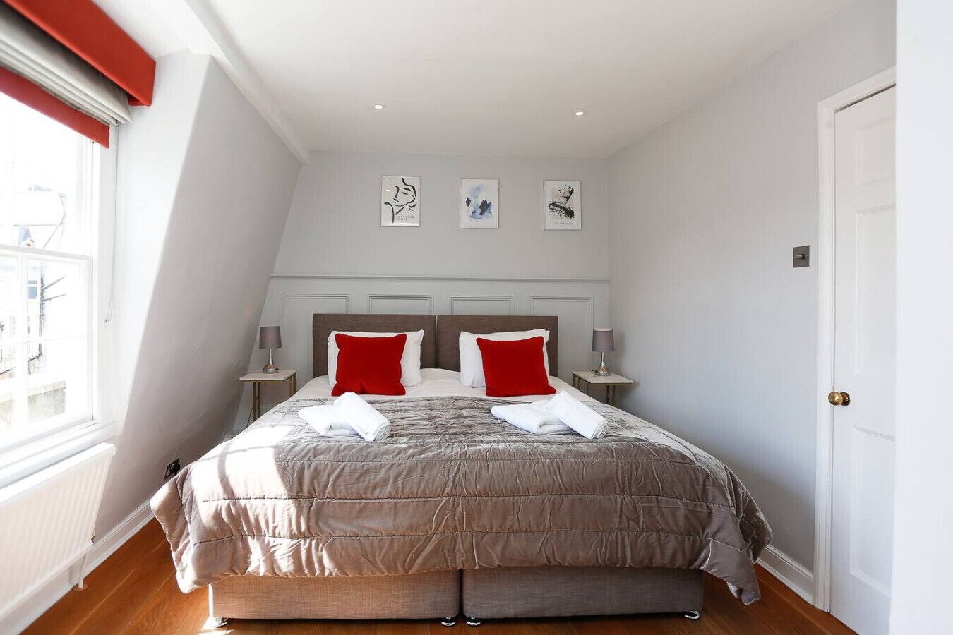 Une chambre à coucher avec un grand lit, deux tables de chevet, une fenêtre et trois œuvres d’art murales.