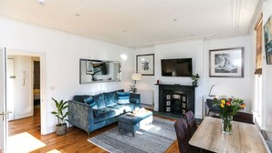 A modern living room with a blue sofa, a wooden dining table, and a fireplace. - Newbridge Road, Spacious One Bedroom (Bath)