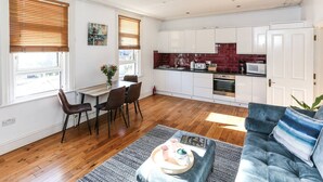 A modern kitchen with white cabinets, a red backsplash, and a dining area with a table and chairs. - Newbridge Road, Spacious One Bedroom (Bath)