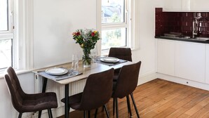 A dining area with a table set for four, chairs, a vase with flowers, and a view of the kitchen. - Newbridge Road, Spacious One Bedroom (Bath)