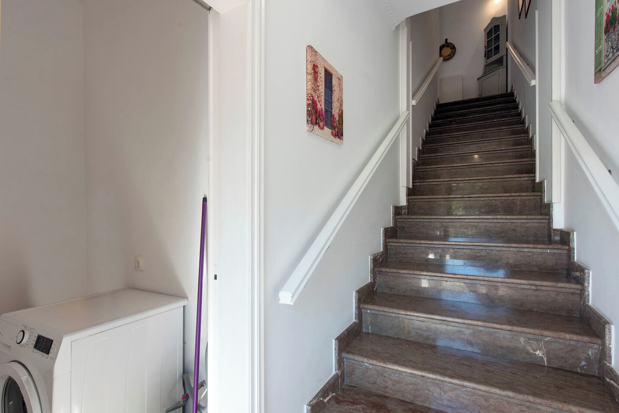 A staircase with a handrail and a washing machine in the adjacent room.