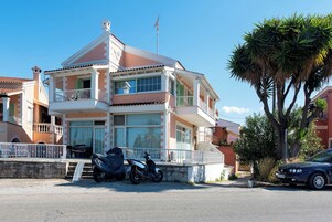 Un edificio residencial de varios pisos con balcones, una motocicleta estacionada y un coche.