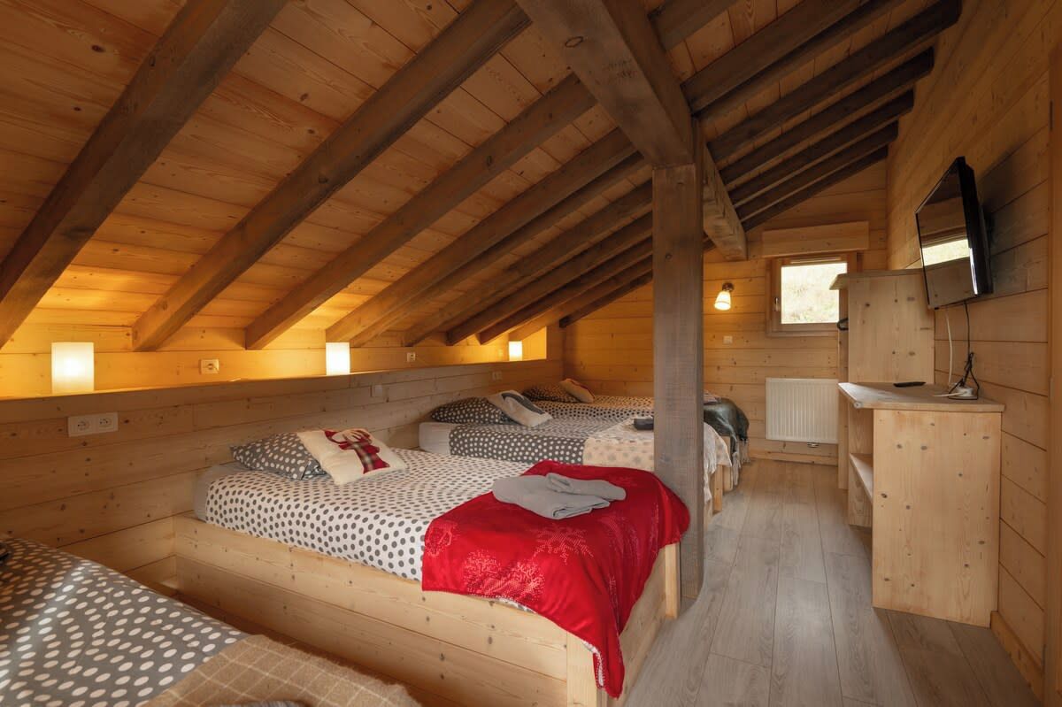 Ein gemütliches Schlafzimmer im Dachgeschoss mit Holzbalken, einem Bett mit roter Decke und einem kleinen Schreibtisch mit Spiegel.