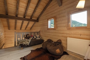 Interior acogedor de una cabaña con techo de madera, un sofá con peluches, una ventana con vistas y un radiador.