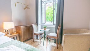 A hotel room with a bed, a small table with chairs, a radiator, and a window with curtains. - Chic Room with Private Bath | Mariahilferstraße (Vienna)