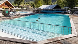 Piscina retangular com deck de madeira ao redor, um posto de salva-vidas e cadeiras de descanso.