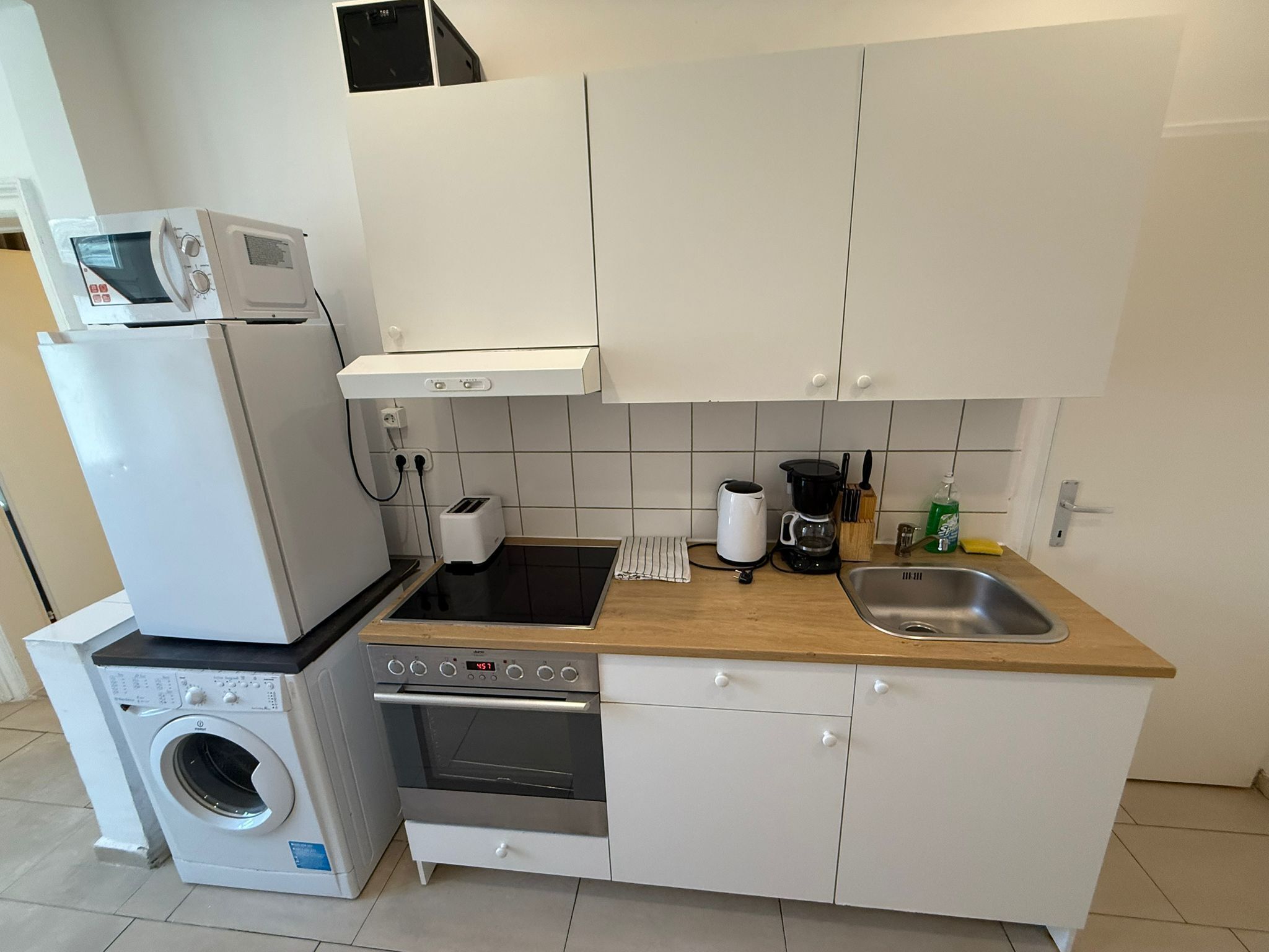 A compact kitchen with a washing machine, microwave, oven, and a coffee maker.