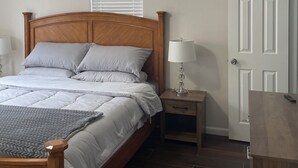 A bedroom with a wooden bed, a nightstand with a lamp, a ceiling fan, and a white door.