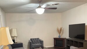 A living room with a sofa, armchair, TV, and a ceiling fan.