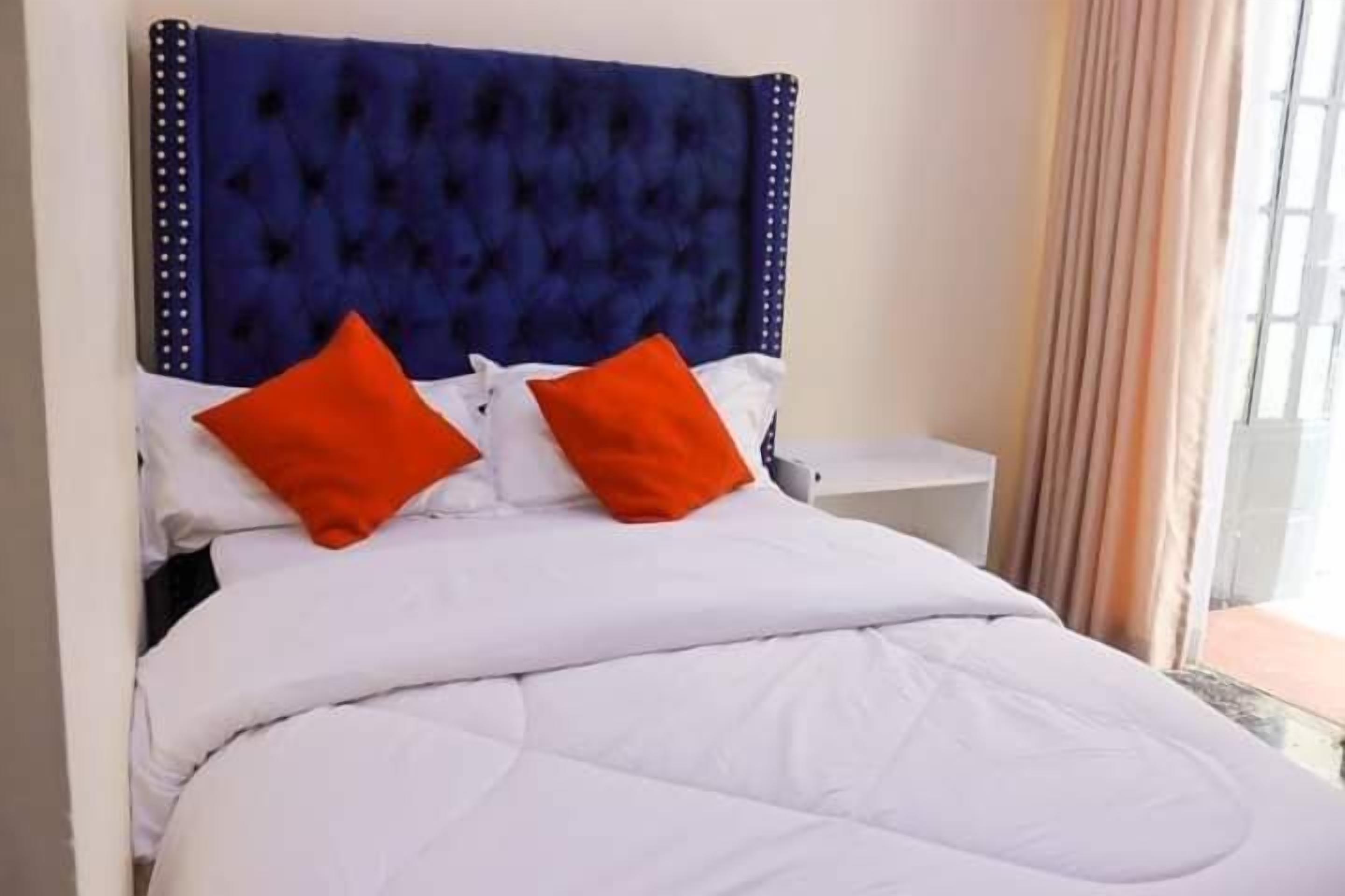 A bed with a tufted headboard, white bedding, and two orange pillows.