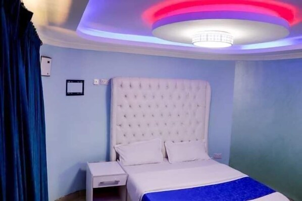 Une chambre à coucher avec une tête de lit capitonnée, un lit simple avec une literie blanche, une table de chevet et une petite table d’appoint.