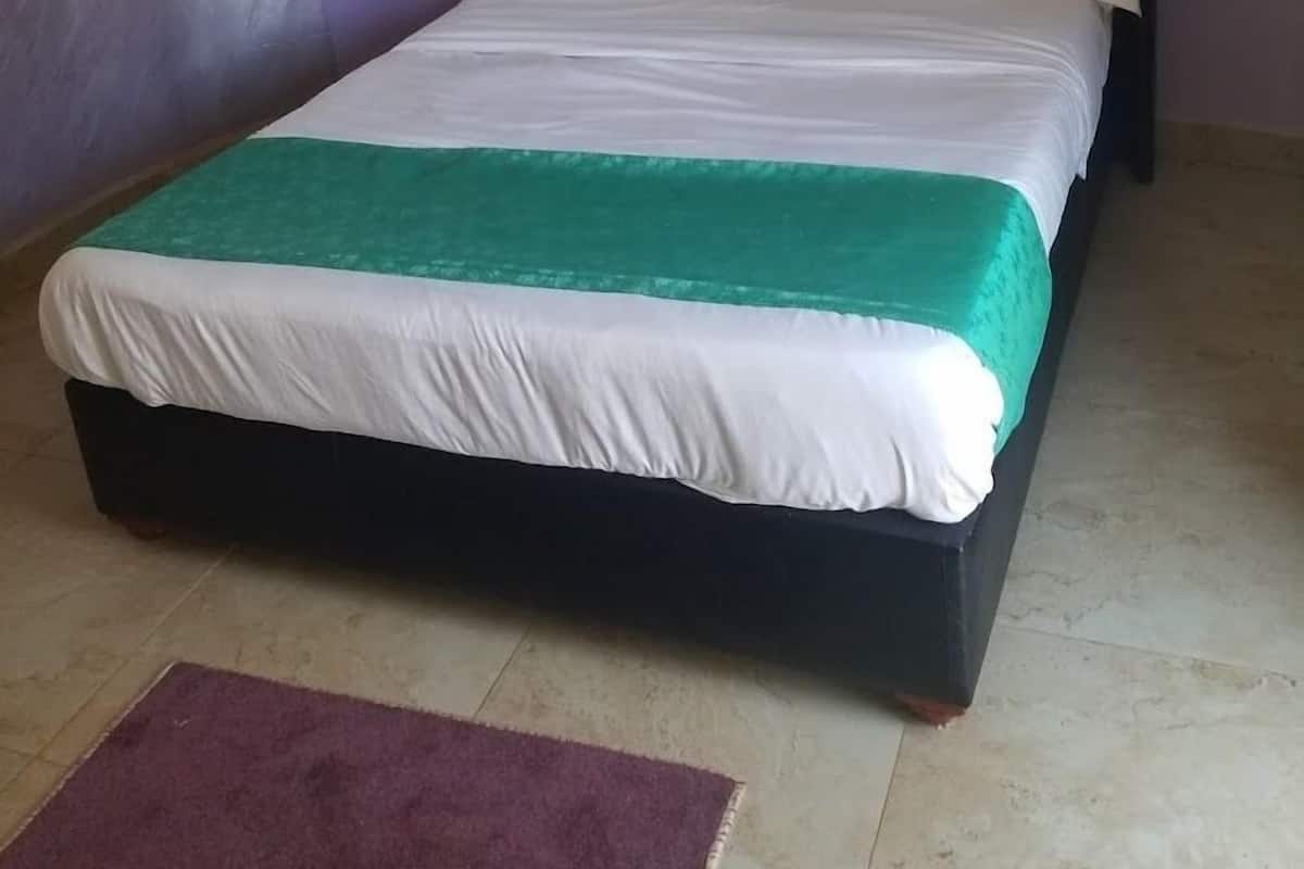 A bed with a dark headboard, white bedding, and a green throw.