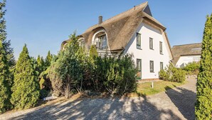 A house with a unique thatched roof, a paved driveway, and a sign indicating a parking area.