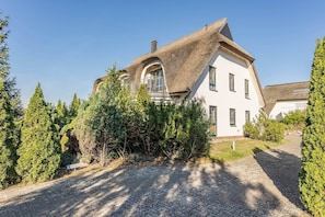 Une maison dotée d’un toit de chaume original, d’une allée pavée et d’un panneau indiquant un espace de stationnement.