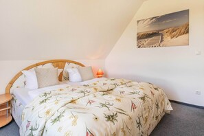 Une chambre à coucher avec un lit, des oreillers, une table de chevet, une lampe et un tableau accroché au mur.