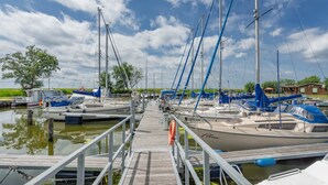 A marina with boats docked, a wooden walkway, and a clear sky.