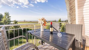 A balcony with a table, wicker chairs, a bottle of wine, and a vase of flowers.